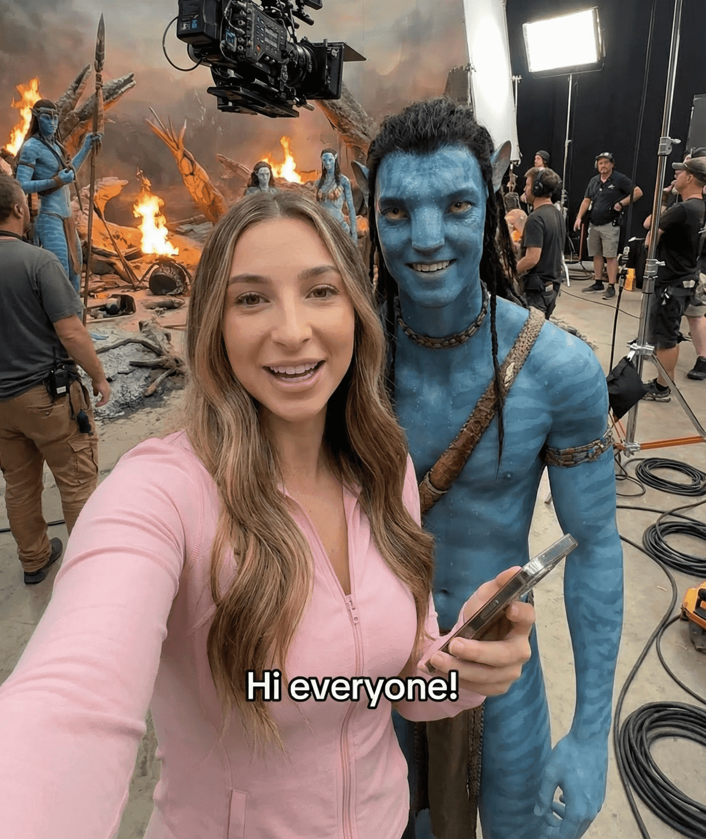 Girl in pink shirt standing next to Jake Sully in Avatar form taking a selfie behind the scenes on the movie set